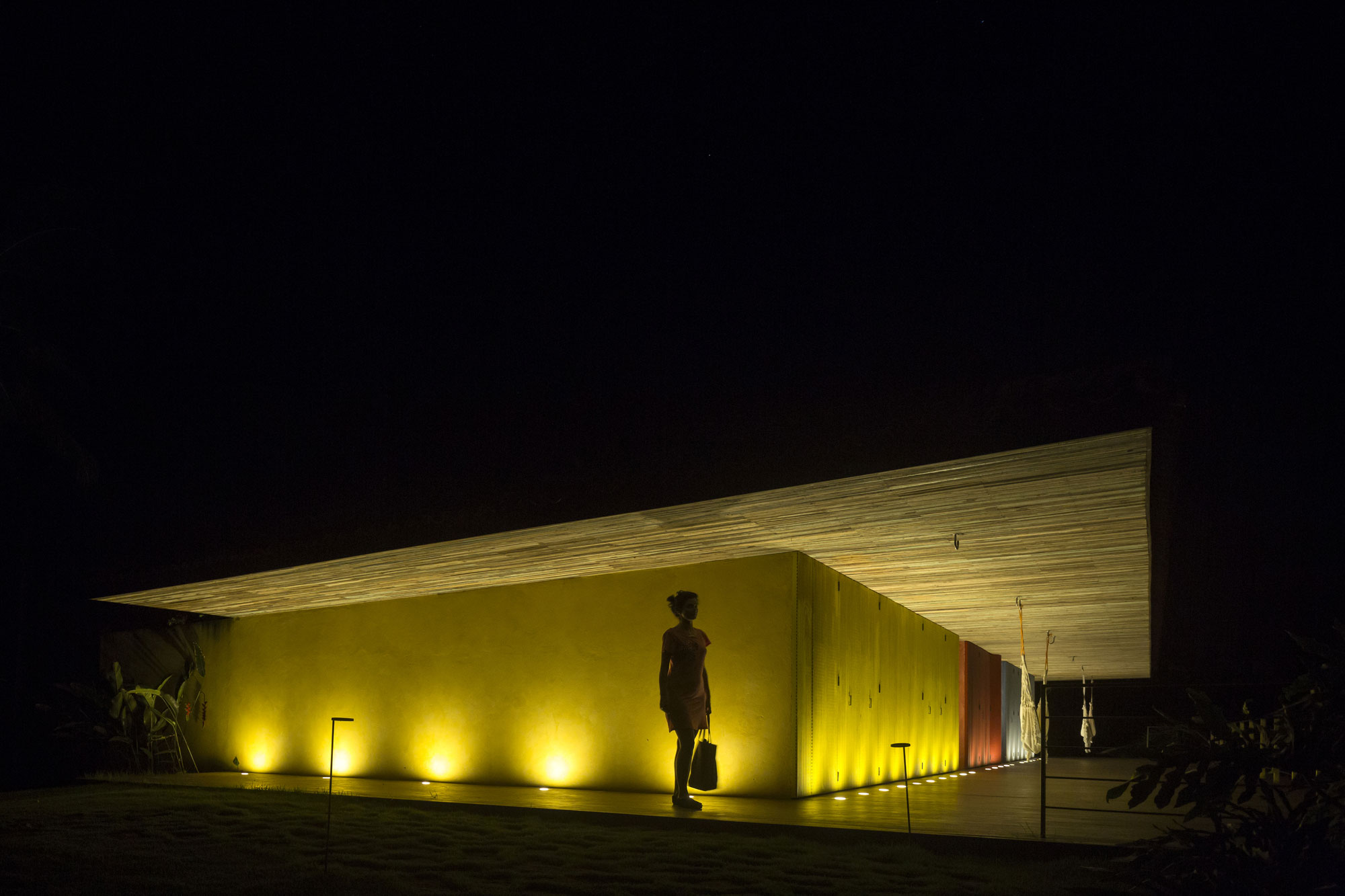 Проект каскадного домика Txai House: жёлтый фасад при ночном освещении